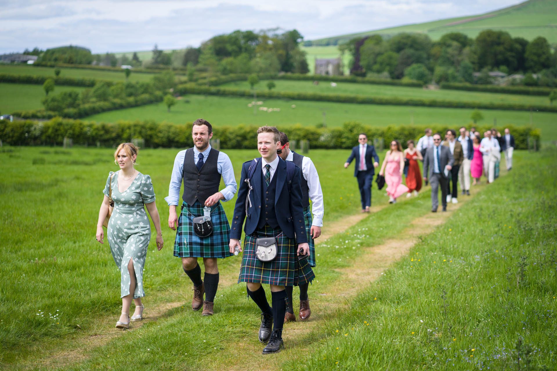 Guests walking across a field to get to Hollie and Colin's Scottish Borders wedding after being dropped off from the coach