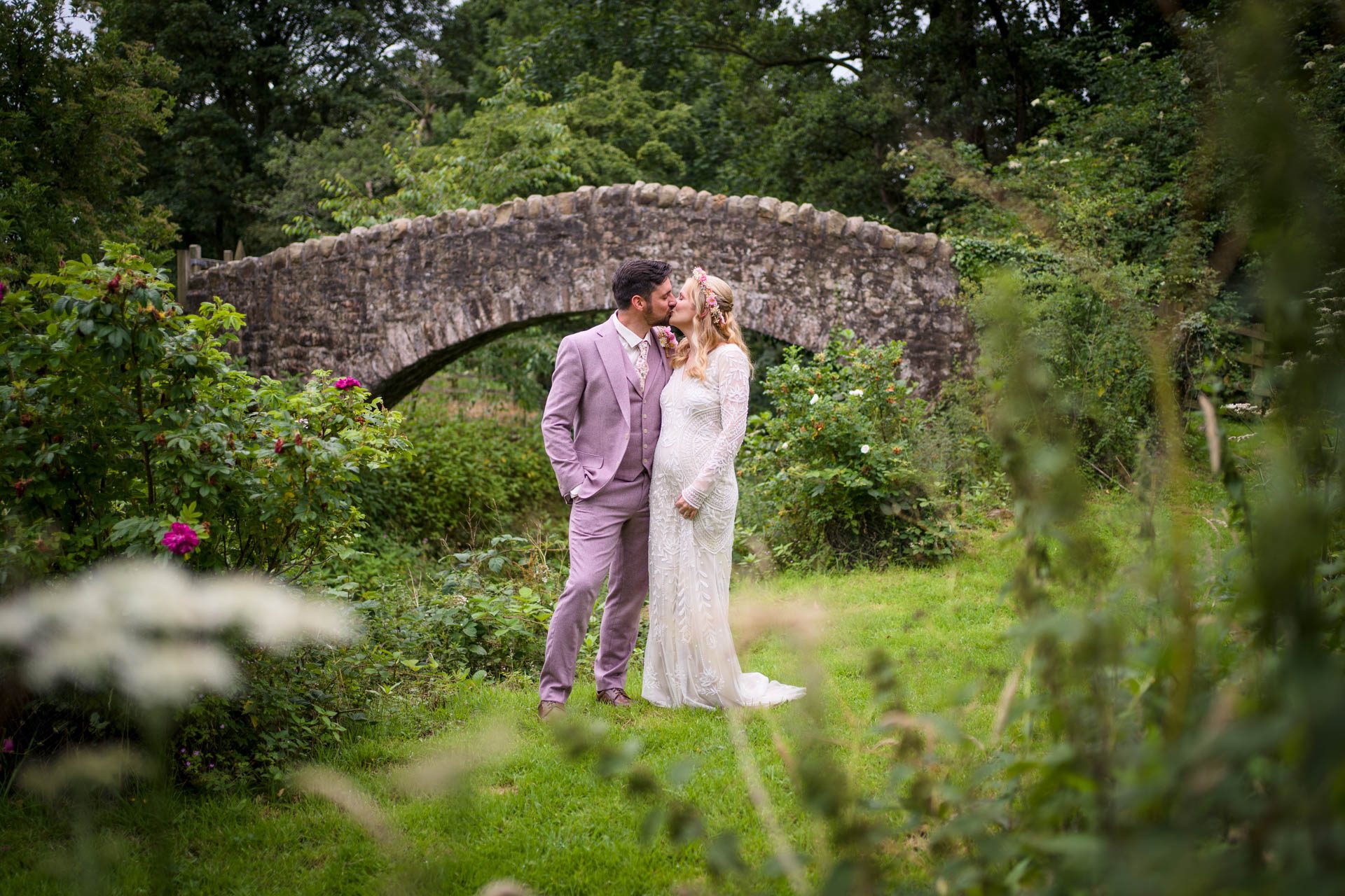 Wedding portrait at Ribble Valley wedding - bride and groom kissing in front of ancient arched stone bridge 