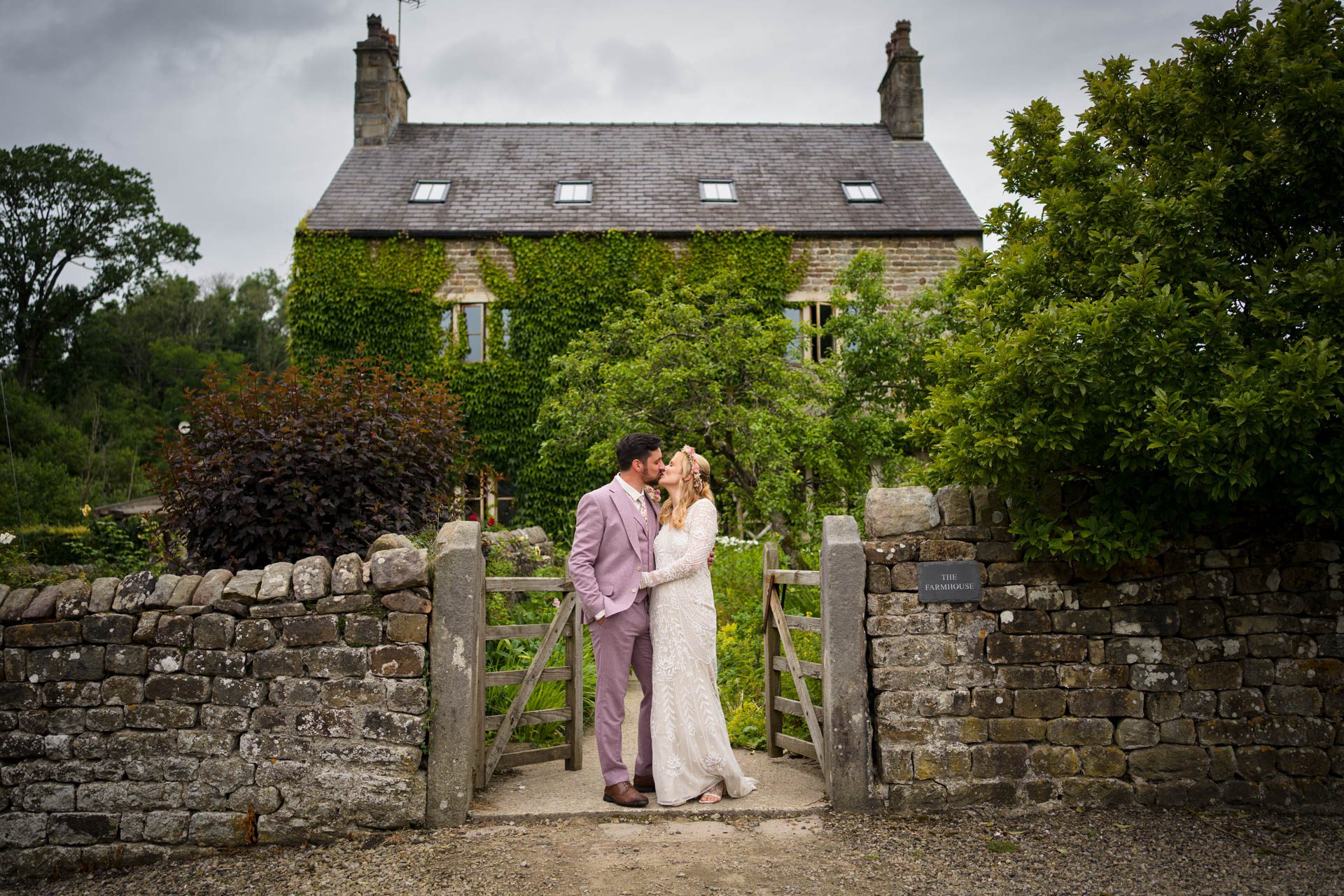 Wedding portrait - bride and groom kissing in front of The Farmhouse at Clough Bottom